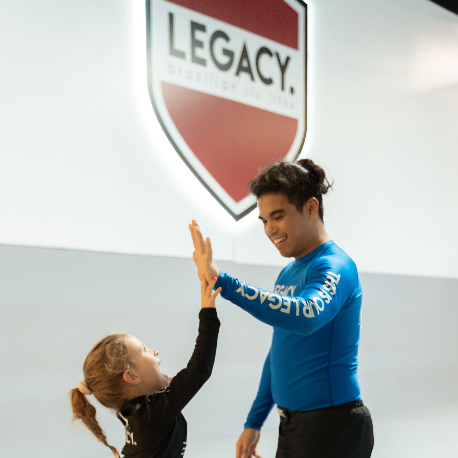 Coach and student high-fiving in front of the Legacy shield